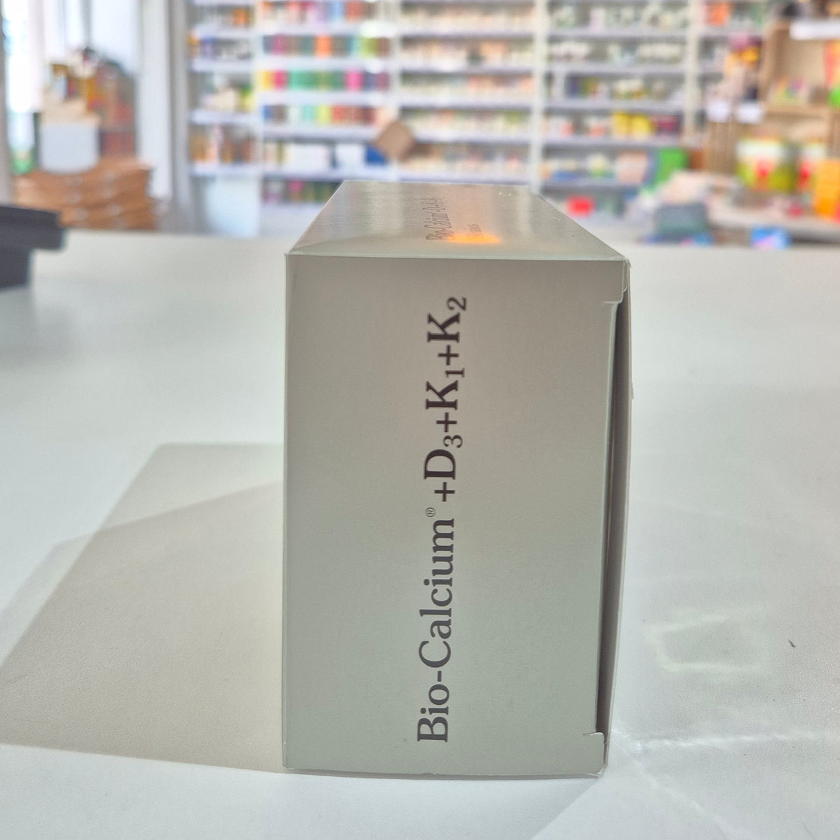Box labeled 'Bio-Calcium + D3+K2' in a store setting with blurred shelves in the background.