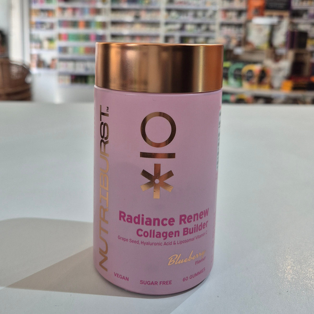 Pink supplement container with gold lid on a white surface, blurred store shelves in the background