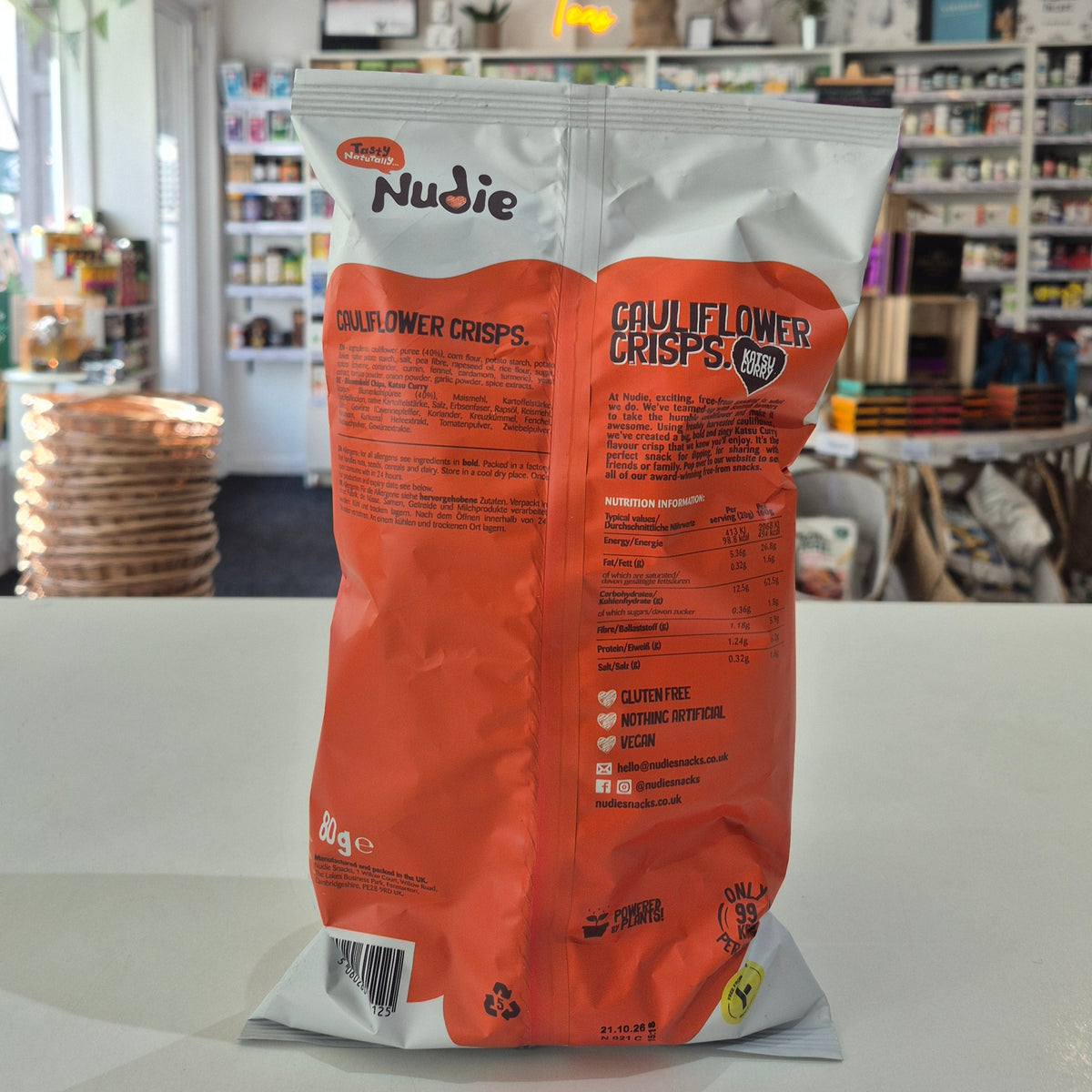 Nudie Cauliflower Crisps packaging on a white surface with a blurred store background