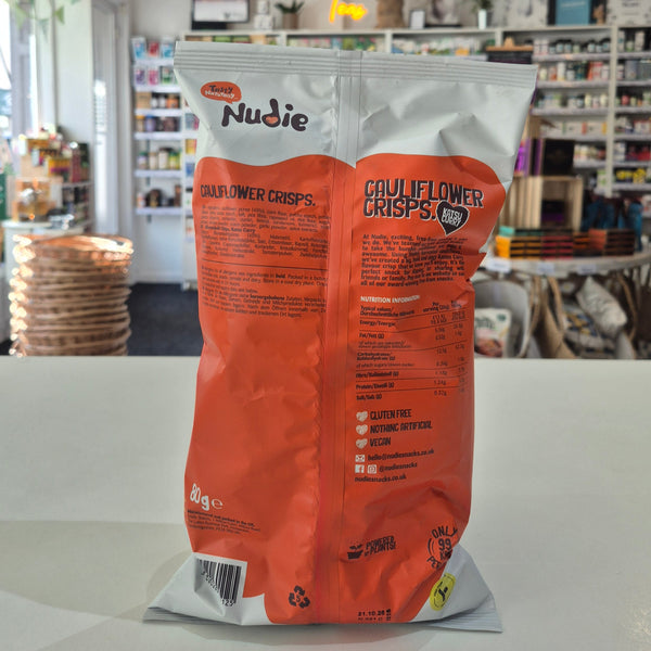 Nudie Cauliflower Crisps packaging on a white surface with a blurred store background