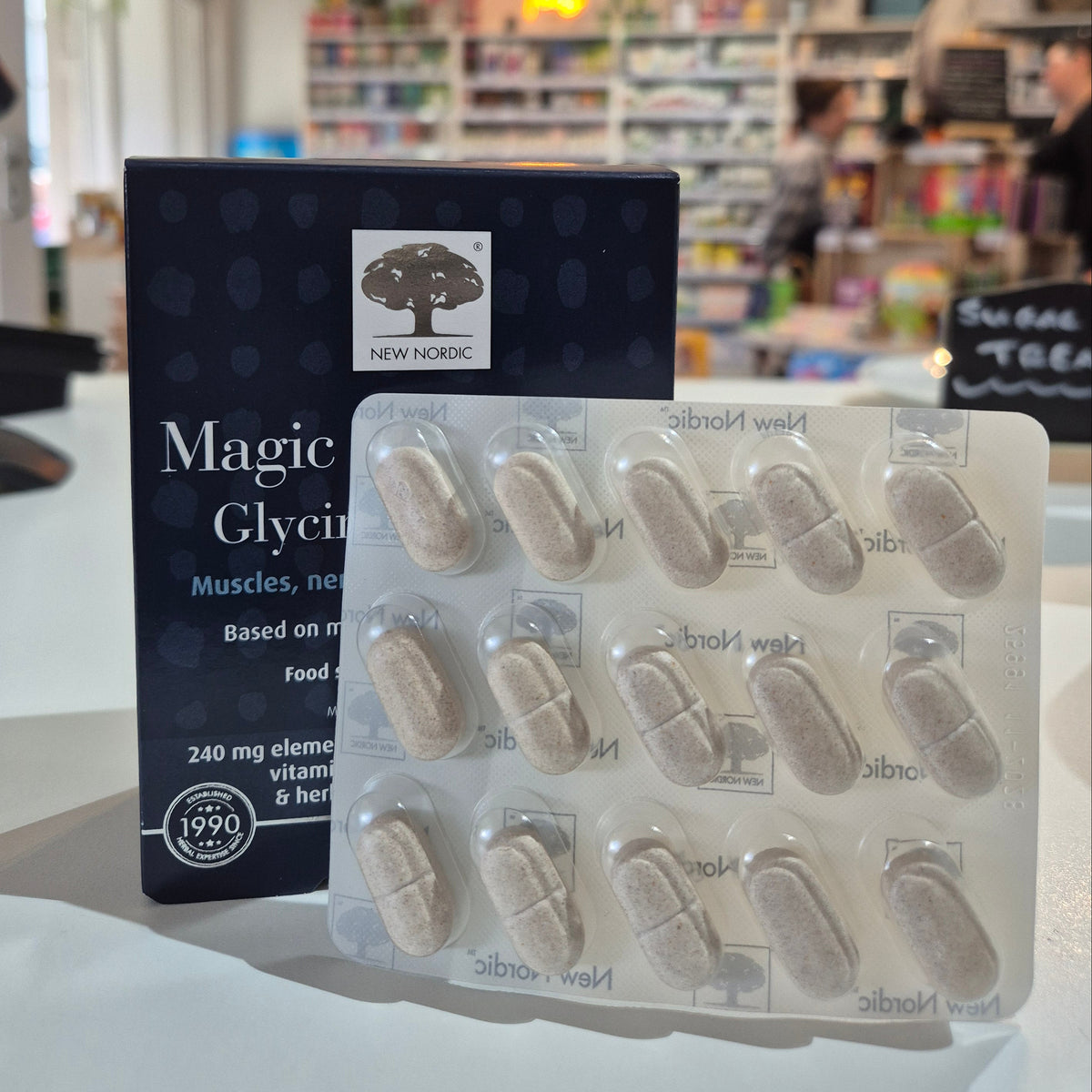 Box of New Nordic Magic Magnesium Glycinate 600 mg supplement on a blurred store shelf background. Packaging of New Nordic Magic Glycine capsules in a pharmacy setting