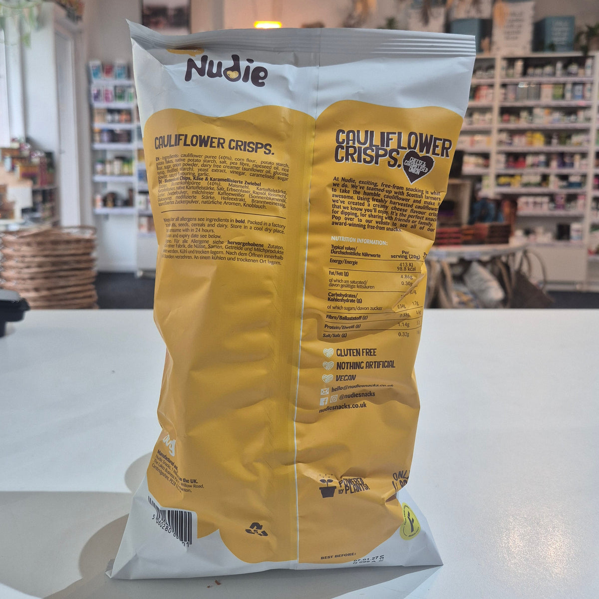 Yellow and white package of Nudie Skins on a white surface with a blurred indoor background