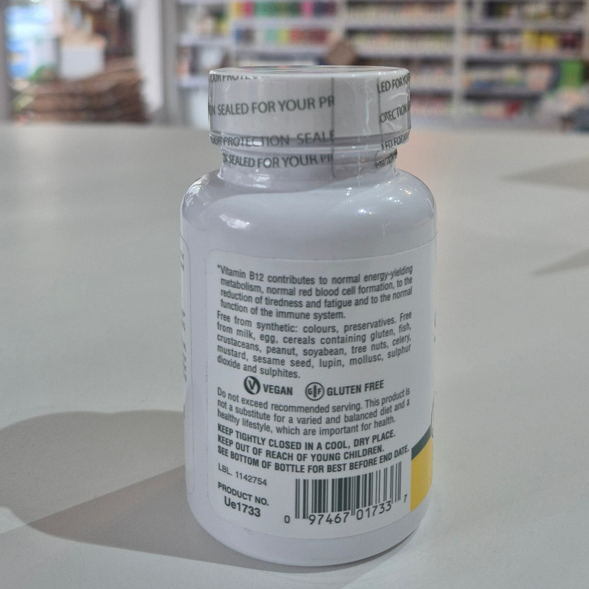 Nature's Plus Shot-O-B12 5000 Mcg lozenge in a white bottle with green and purple label, indicating wild berry flavor and dietary supplement category. Supplement bottle with label on a blurred store shelf background
