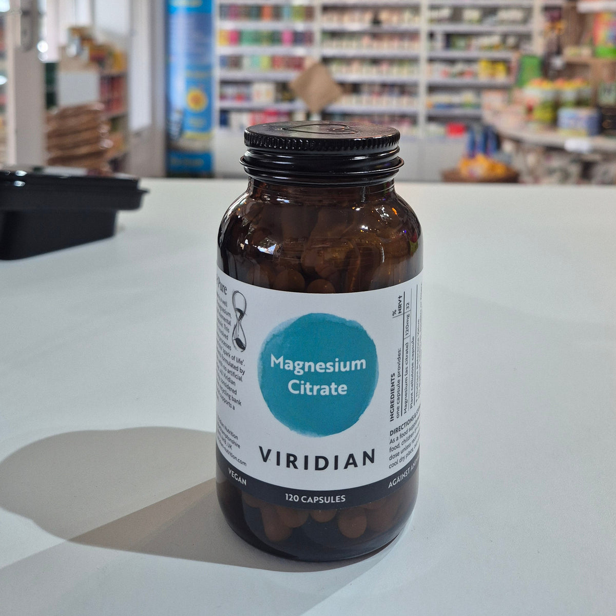 Magnesium Citrate in a bottle with a label on a white surface, blurred store interior in the background