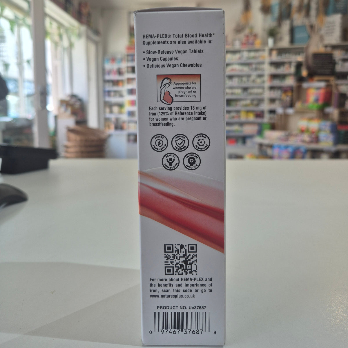 Box of NaturesPlus Hema-Plex Liquid Iron supplement on a counter with QR code and text on a blurred store background