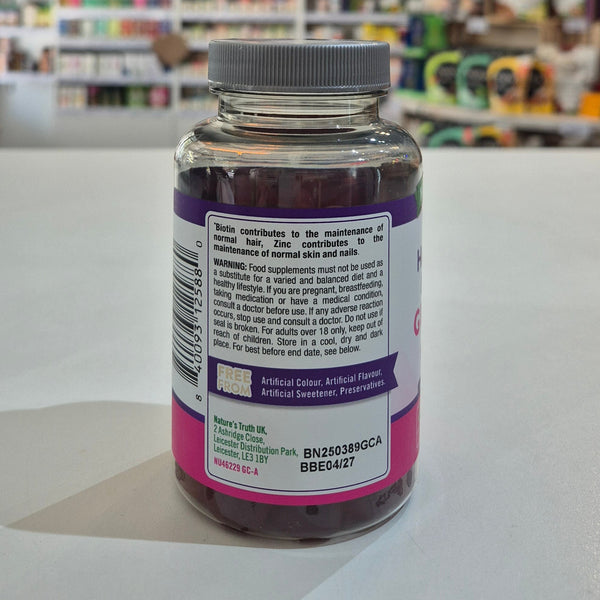 Nature's Truth Hair, Skin & Nails Gummies bottle on a white surface with a blurred store background. Supplement bottle with label on a white surface in a store setting