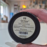 Hand holding a jar of Oat Soap Intensive Balm with a blurred indoor background