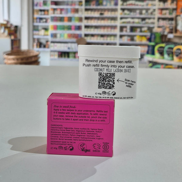 Pink deodorant refill box labeled 'fussy' on a counter with a store background. Pink and white containers with text and a QR code on a surface with a store background