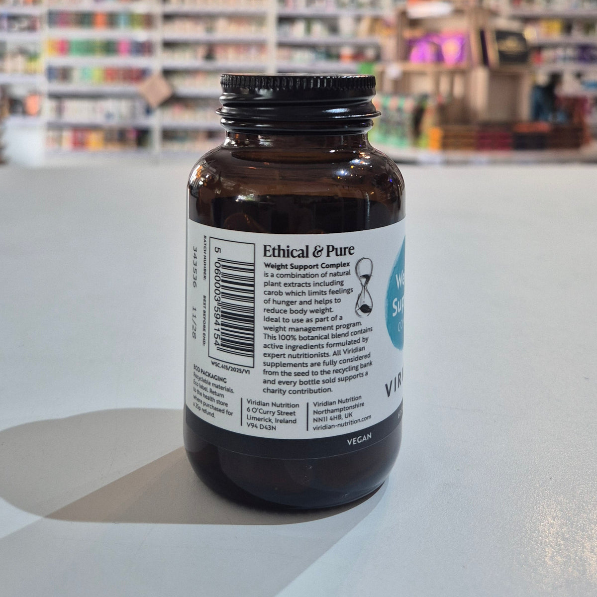 Brown supplement bottle with label on a white surface, blurred store shelves in the background
