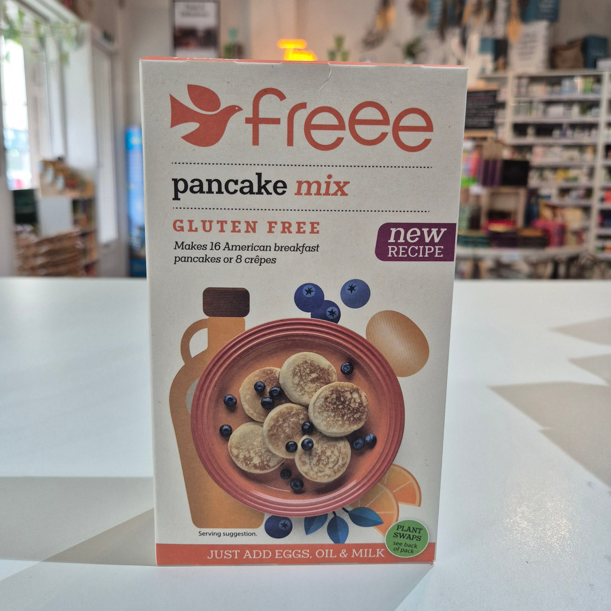Box of gluten-free pancake mix with a bowl of pancakes and blueberries on the label, held in front of a store shelf.