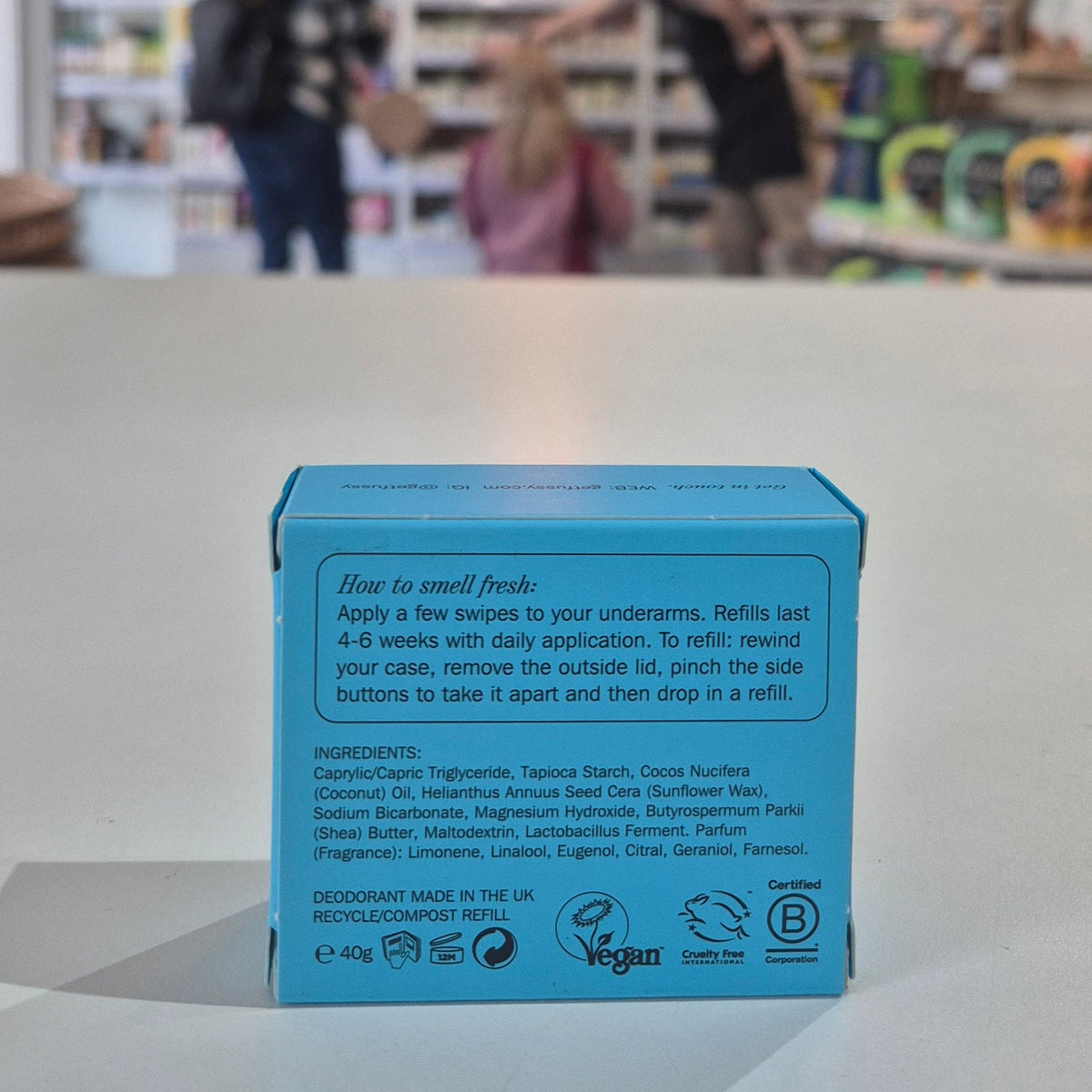 Fussy compostable deodorant refill packaging with a store in the background. Blue deodorant packaging with text and icons on a light surface, blurred store background