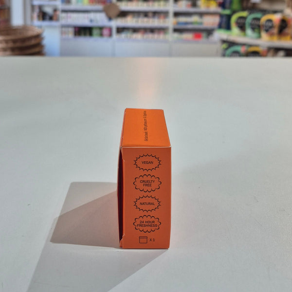 Orange cosmetic box with text on a white surface, blurred store background