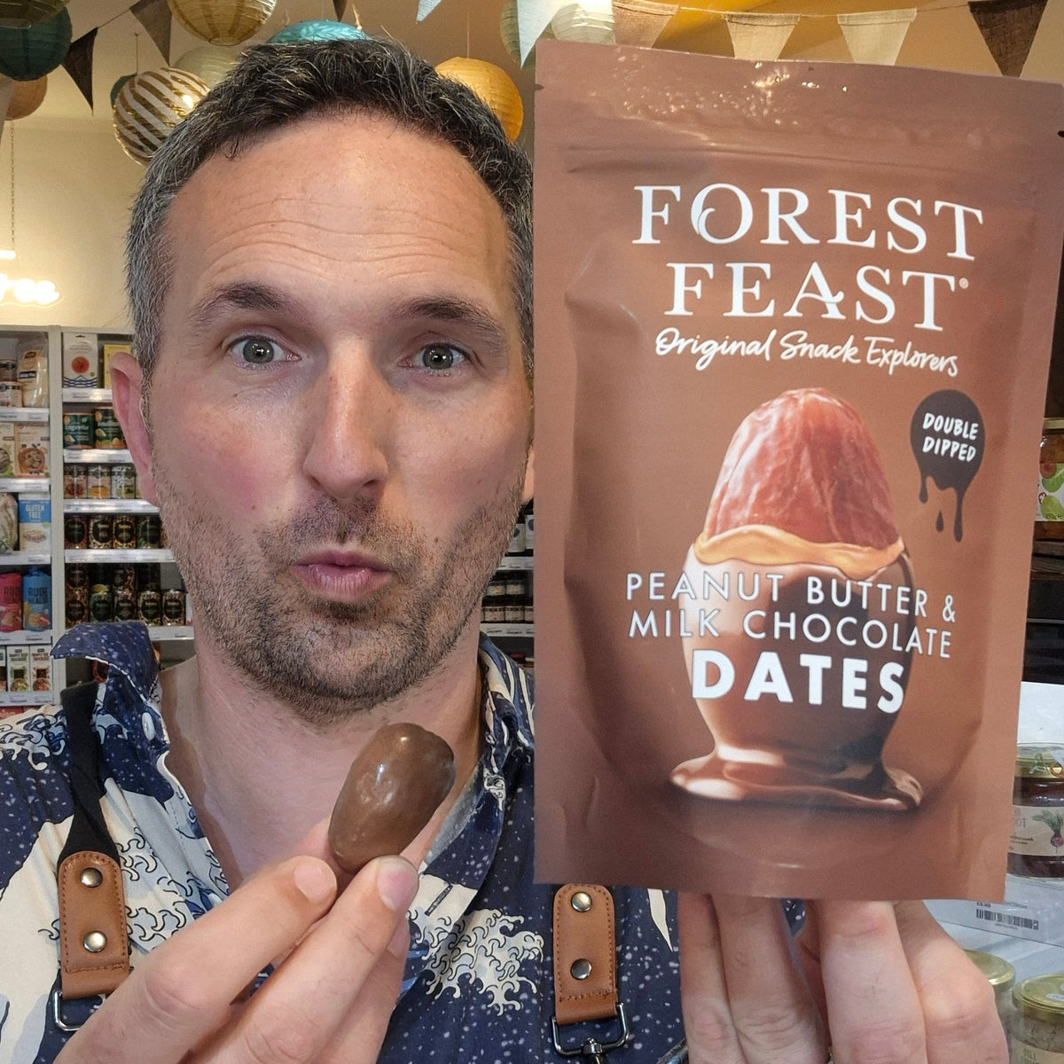 Man holding a chocolate date and a 'Forest Feast' Peanut Butter and Milk Chocolate package in a store setting