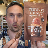Man holding a chocolate date and a 'Forest Feast' Peanut Butter and Milk Chocolate package in a store setting