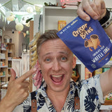 A smiling man in a tropical print shirt and a black Health & Remedy apron holds up a blue bag of Crispr Bites Chocolate Filled  Salted Caramel Waffle Cones.