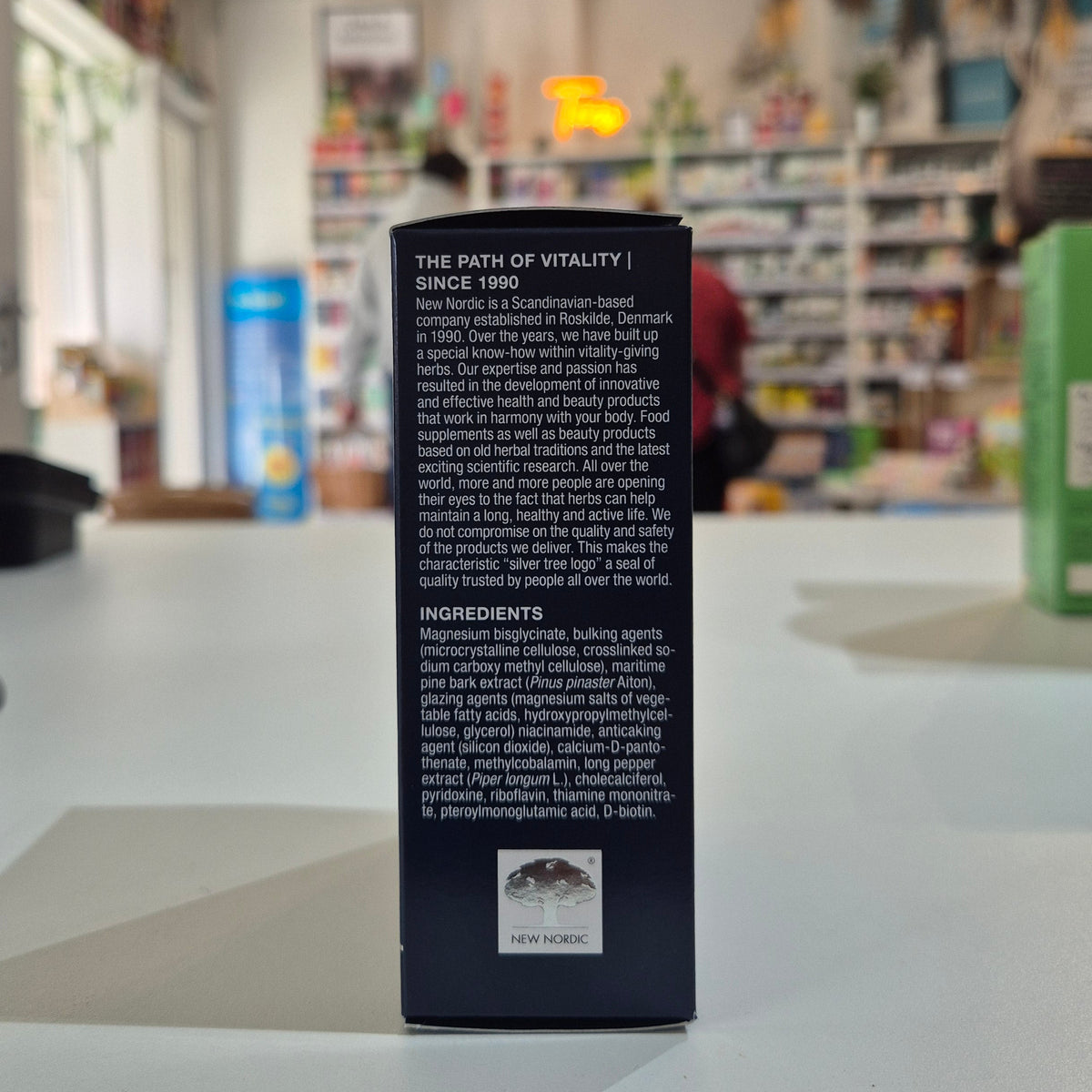 Box of New Nordic Magic Magnesium Glycinate 600 mg supplement on a blurred store shelf background. Back of a product packaging with text on a blurred store background