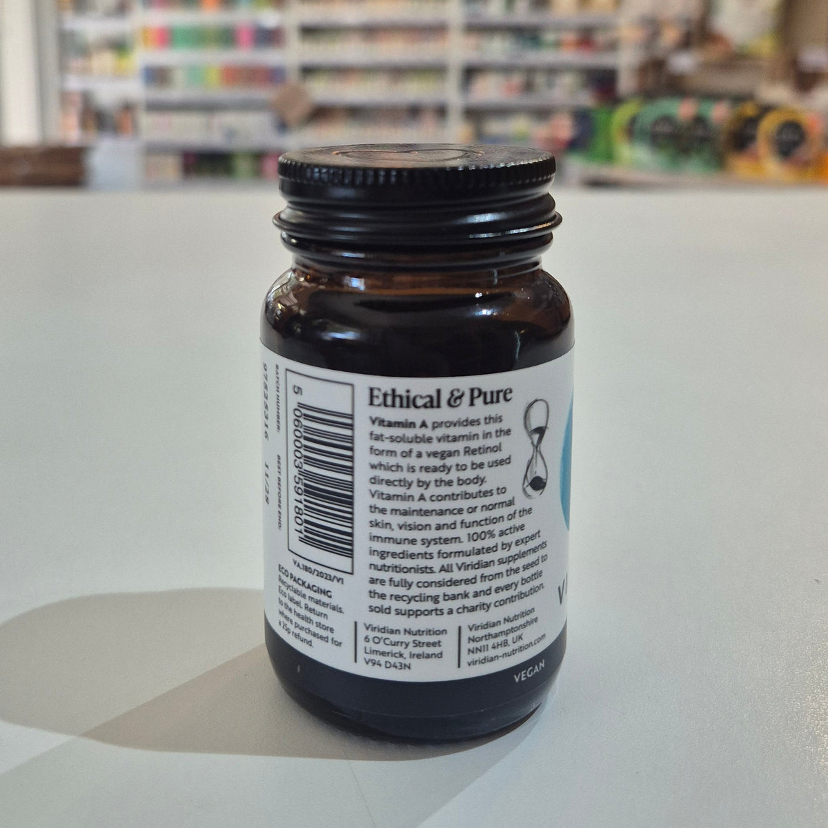 Brown supplement bottle with label on a white surface, blurred store background