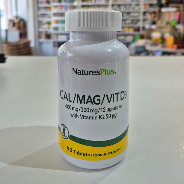 NaturesPlus Cal/Mag/Vit D3 supplement bottle on a table with a blurred store background
