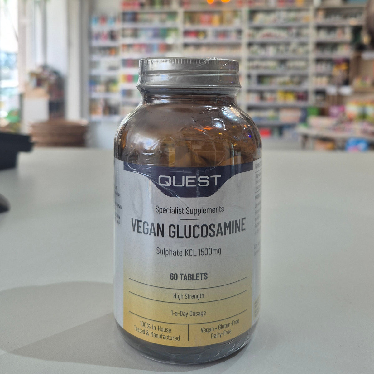 Quest Vegan Glucosamine supplement bottle on a table with a blurred store background