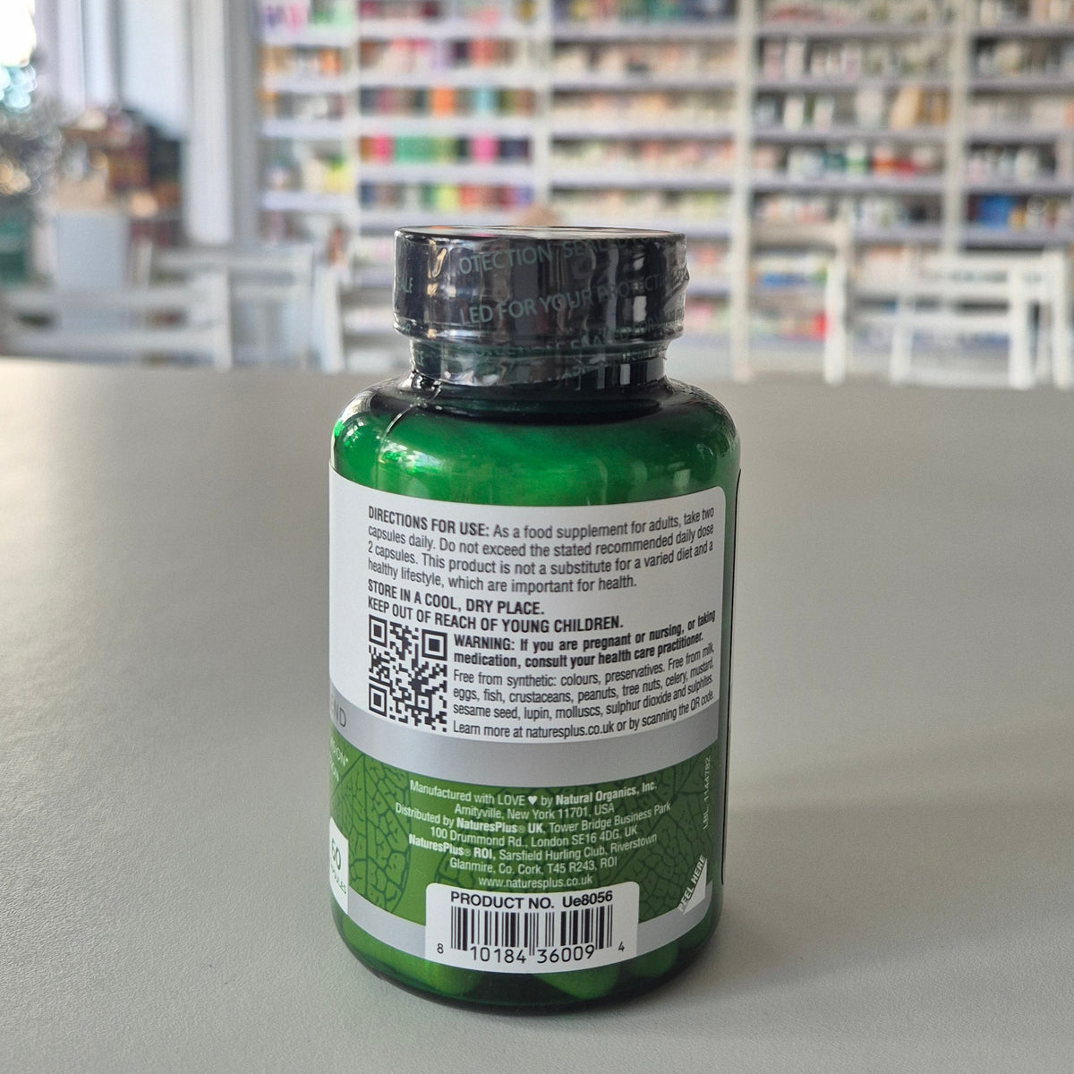 Green supplement bottle with label on a gray surface, blurred background of shelves.