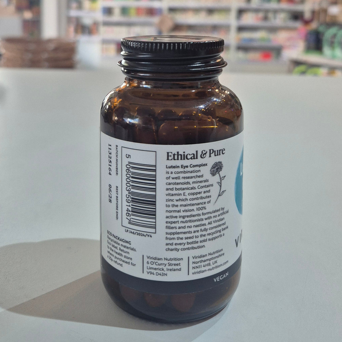 Bottle of Viridian Lutein Eye Complex on a counter with a blurred store background. Brown glass bottle with a label on a white surface, blurred background