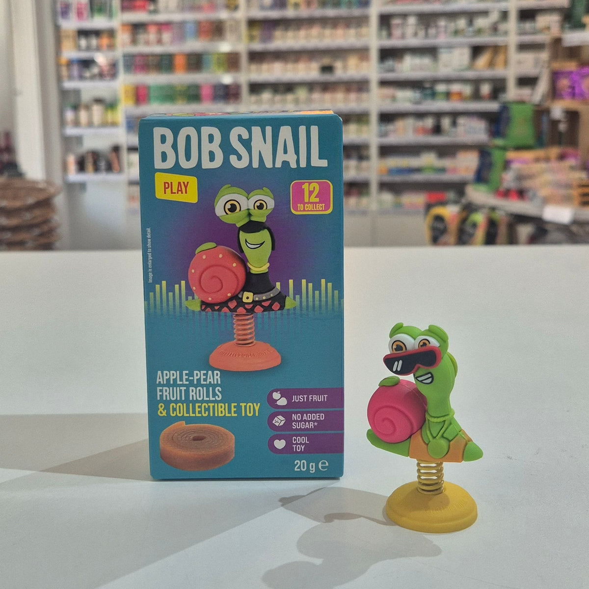 Bob Snail toy and packaging on a table with shelves in the background