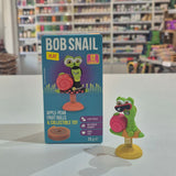 Bob Snail toy and packaging on a table with shelves in the background
