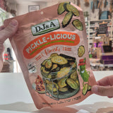 A person holds up a bag of Dj&A Pickle-Licious Kimchi Pickled Zucchini slices in a brightly lit store setting.