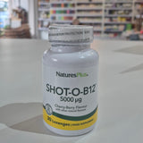 NaturesPlus SHOT-O-B12 supplement bottle on a table with a blurred store background