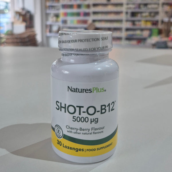 NaturesPlus SHOT-O-B12 supplement bottle on a table with a blurred store background