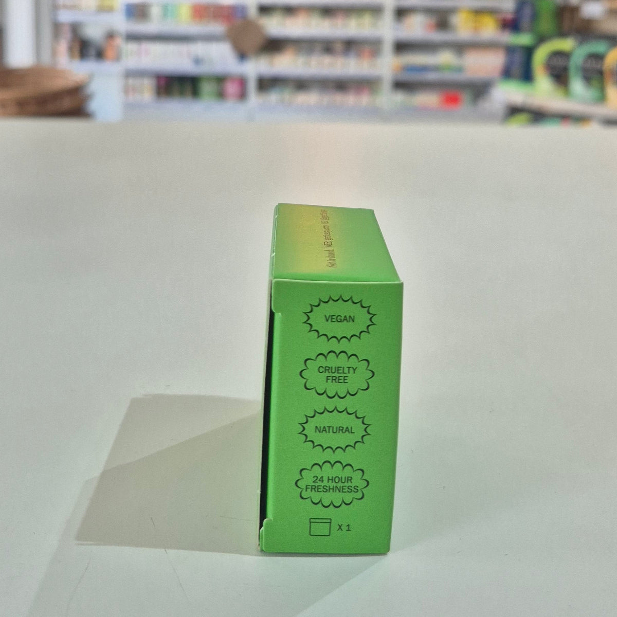 Green product box with certification labels on a white surface, blurred store background